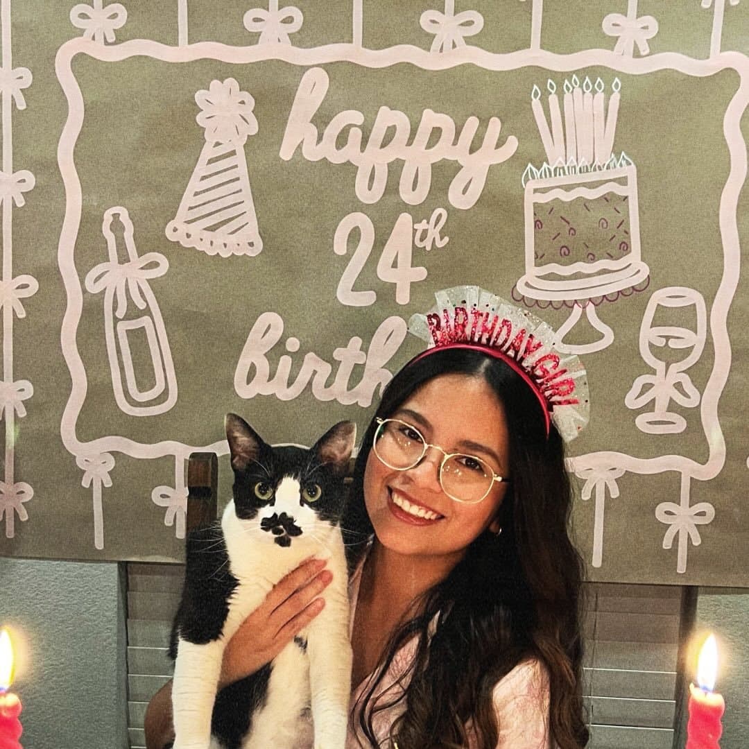 Luisa Quintana โ the artist behind Banners by Luisa, with her cat and one of her hand-painted banners